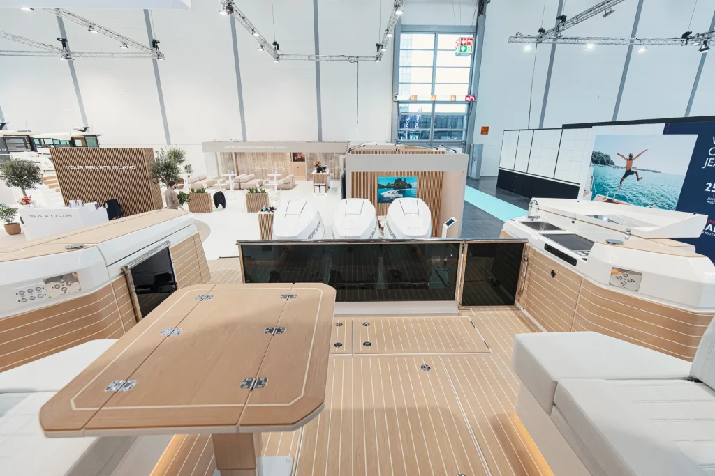 Pozzetto di poppa del Saxdor 460 GTC con tavolo e sedute, vista verso i motori fuoribordo durante esposizione in fiera.