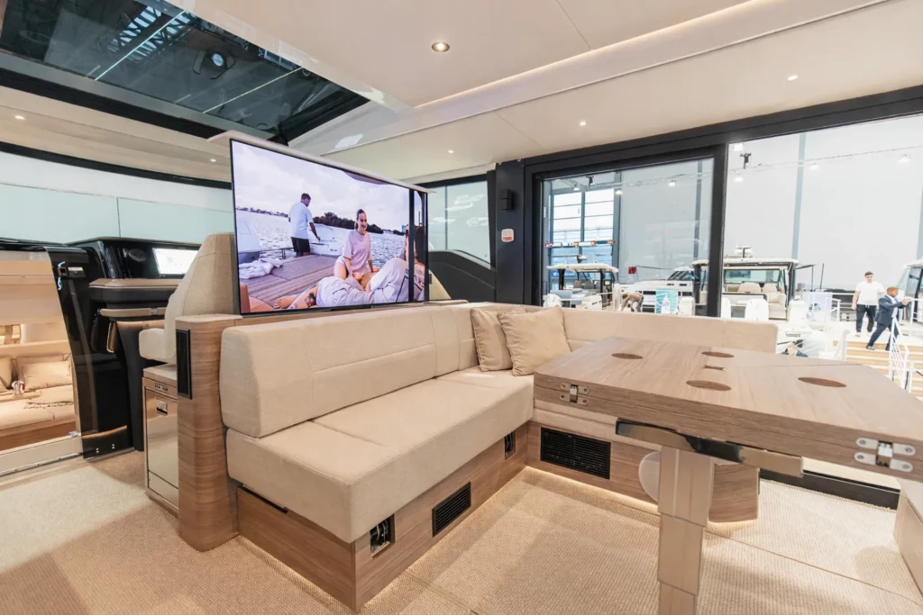 Interni del Saxdor 460 GTC: salone con divano, TV e tavolo dinette in finiture effetto legno e tessuti chiari.